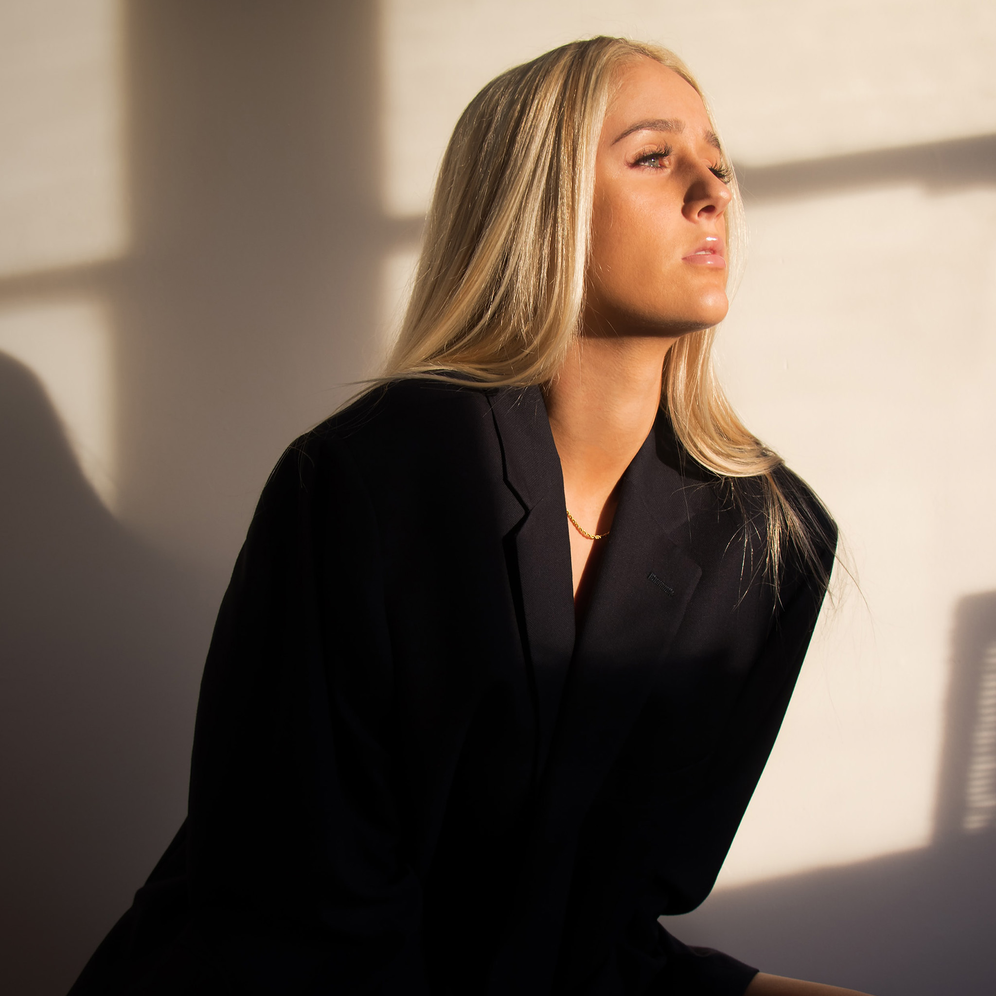 00_lichtfiltering_blonde_vrouw_zwarte_blazer_kijkend_richting_licht_2048x2048