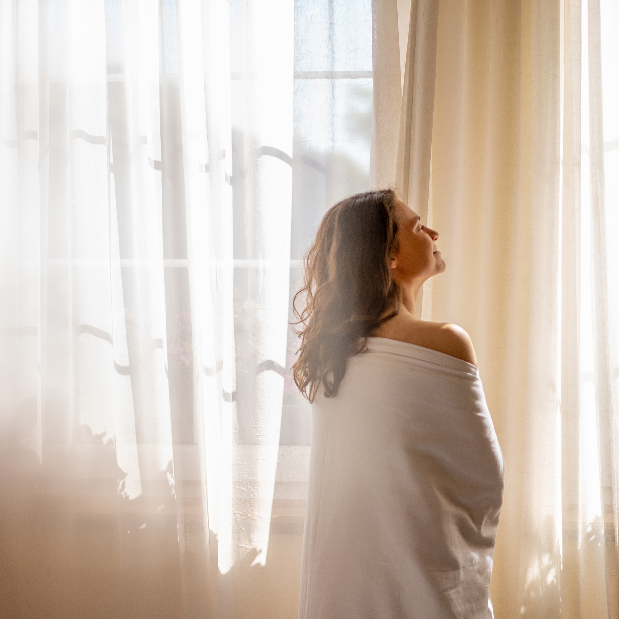 00_lichtfiltering_brunette_in_wit_genietend_van_zon_voor_raam_2048x2048