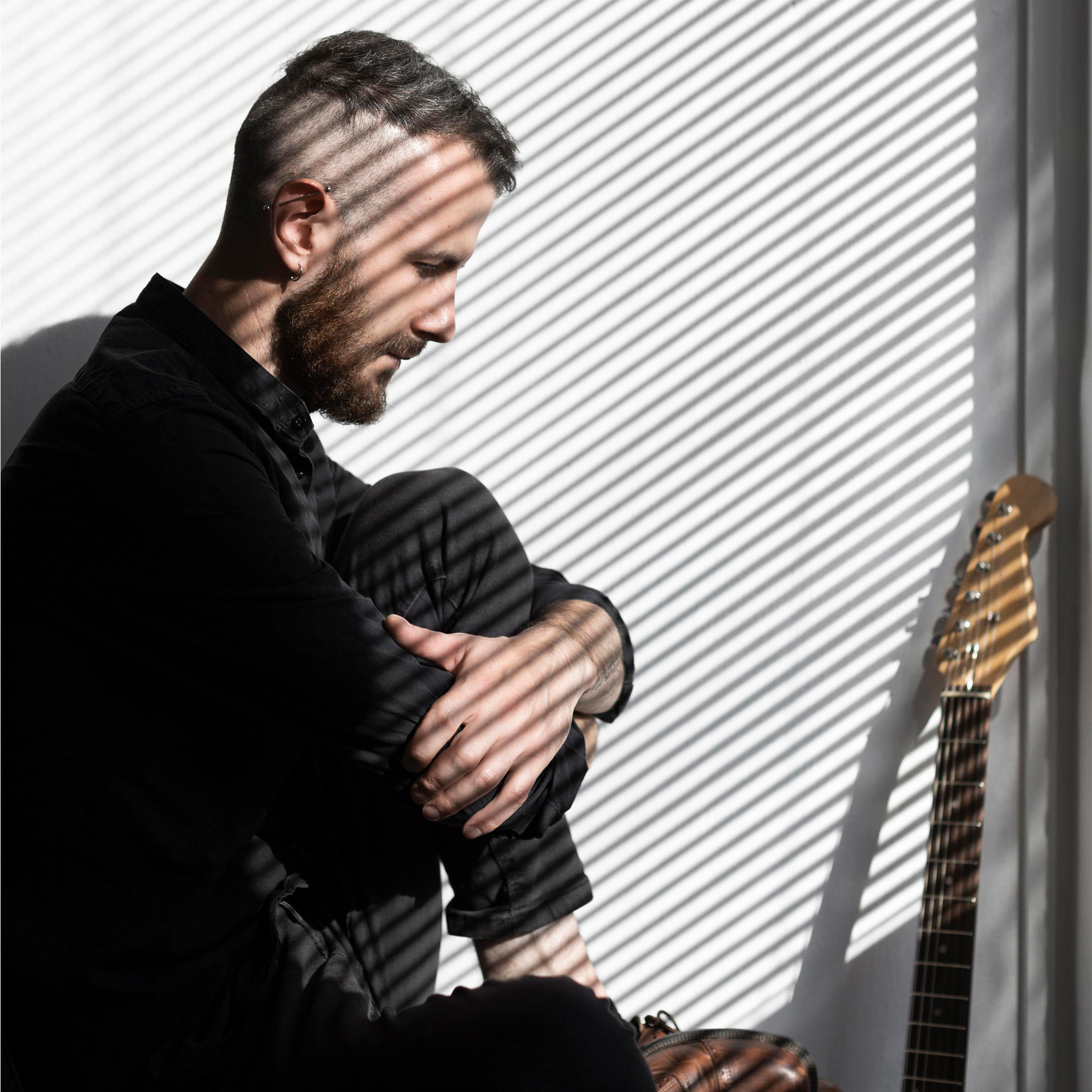 00_lichtfiltering_man_in_zwart_met_gitaar_voor_raam_met_jaloezieen_2048x2048