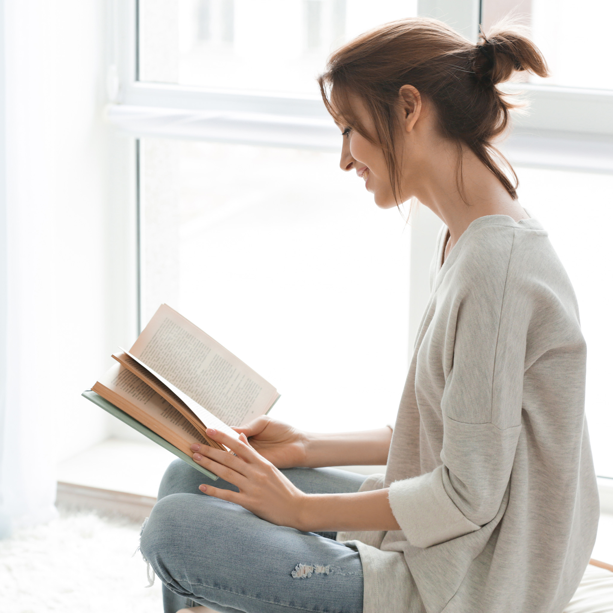 00_onbezorgdheid_brunette_met_knot_leest_boek_in_raamkozijn_2048x2048
